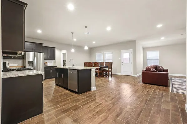a living room with stainless steel appliances kitchen island granite countertop a refrigerator a stove a sink a dining table and chairs with wooden floor