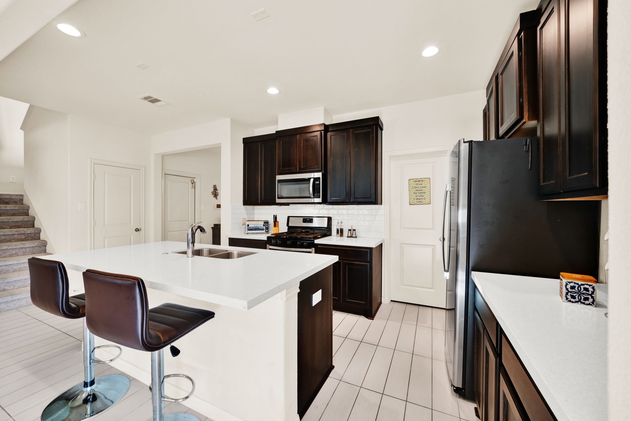 2503 Hagerman Road Conroe, TX 77384 - Photo 11 of 43 This modern kitchen features sleek dark cabinets, stainless steel appliances, and a spacious white island with seating, perfect for casual dining or entertaining.