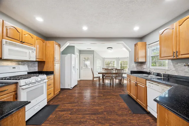 a kitchen with stainless steel appliances granite countertop a stove top oven a sink a dining table and chairs with wooden floor