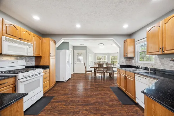 a kitchen with stainless steel appliances granite countertop a stove top oven a sink a dining table and chairs with wooden floor