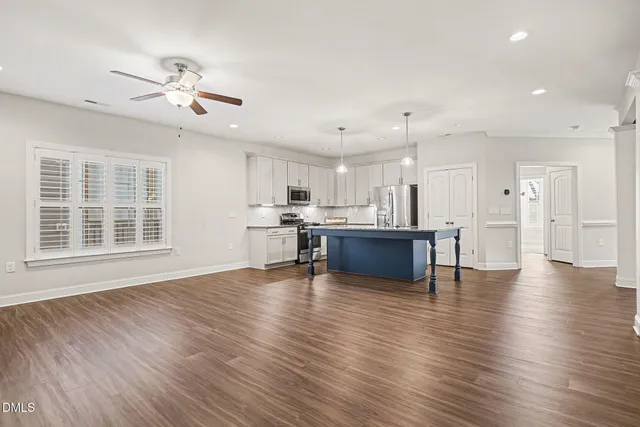 a view of an empty room with wooden floor and a kitchen
