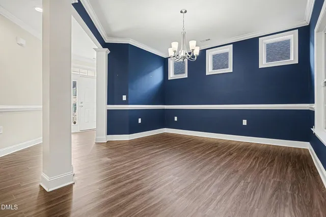 a view of an empty room with wooden floor and chandelier