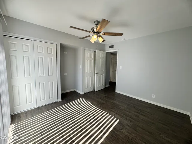 an empty room with wooden floor closet fan and windows