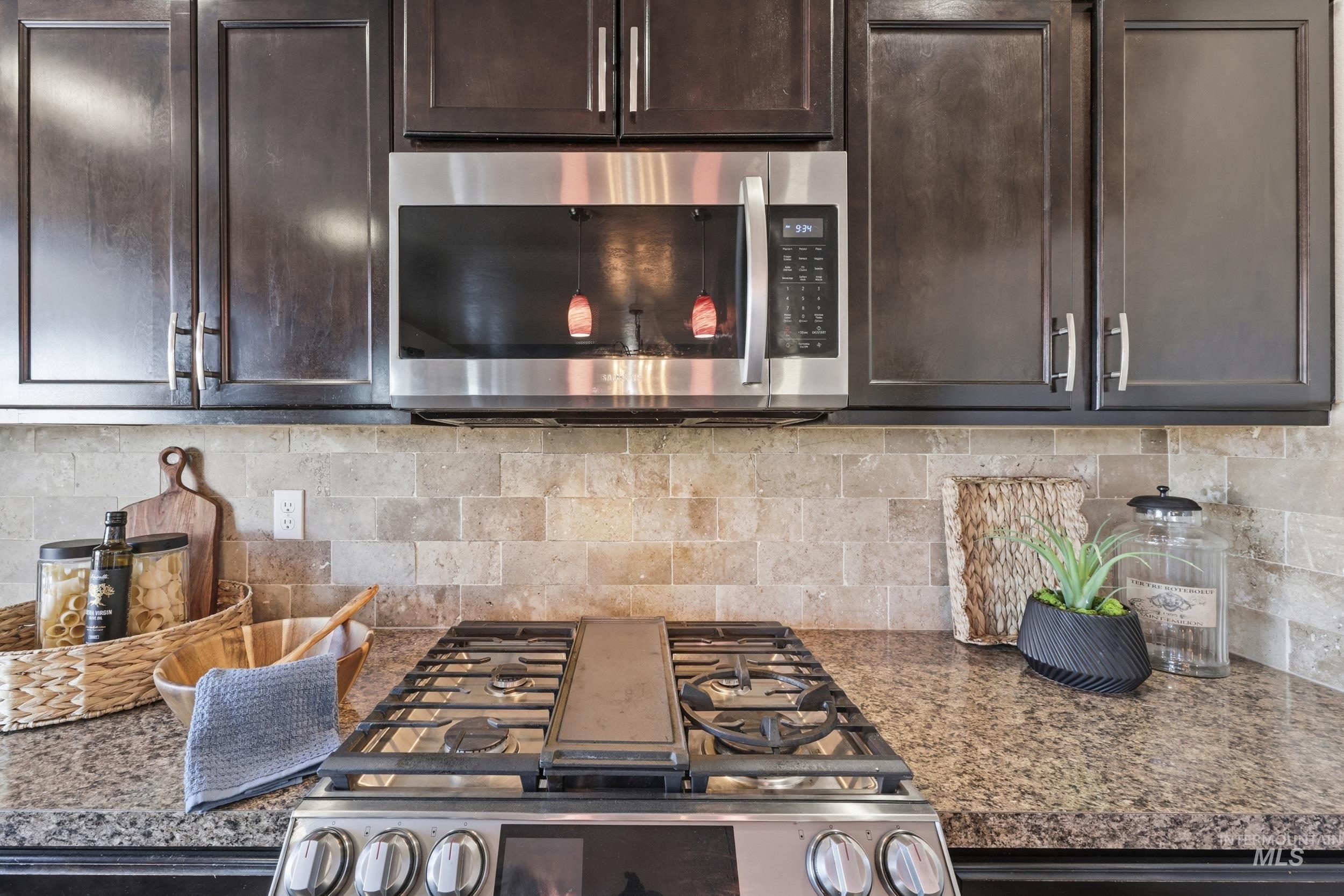 4855 South Chex Way Boise, ID 83709 - Photo 11 of 47 Kitchen featuring dark wood cabinetry, stainless steel microwave, stone tile backsplash, and a gas range