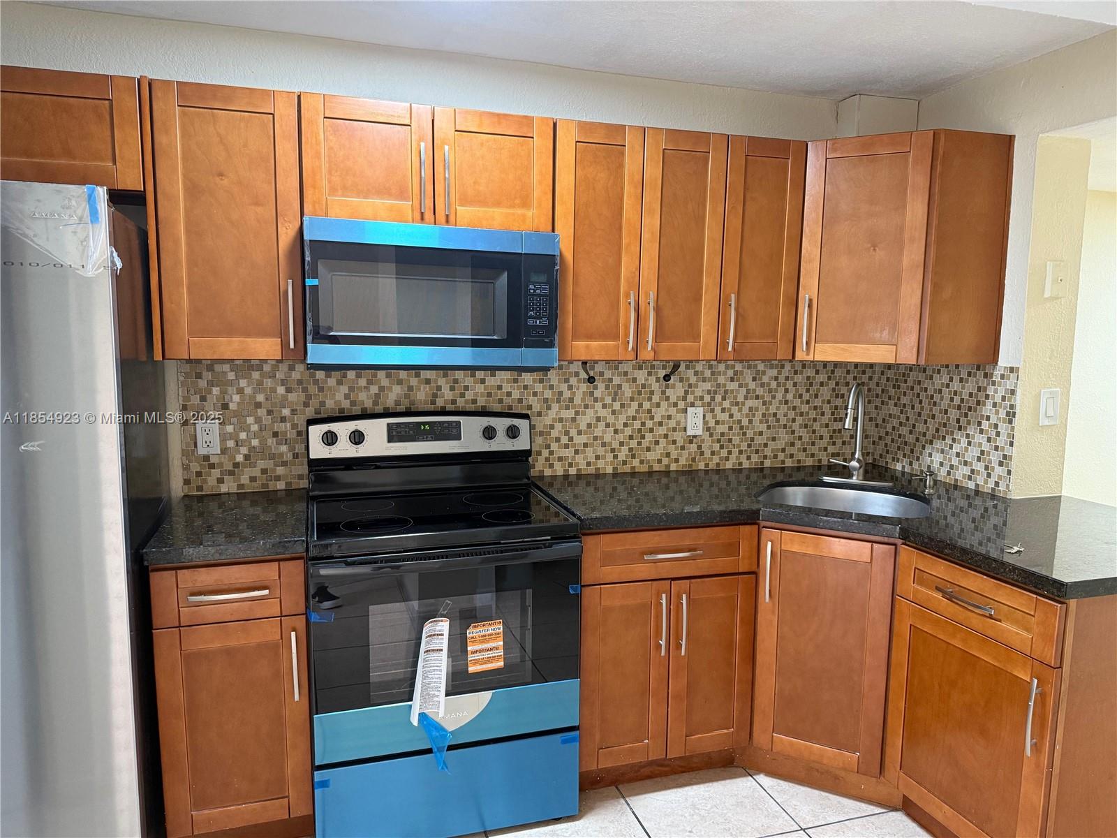 2310 West 60th Street, Unit 9G Hialeah, FL 33016 - Photo 5 of 15 a kitchen with granite countertop a stove top oven microwave and cabinets
