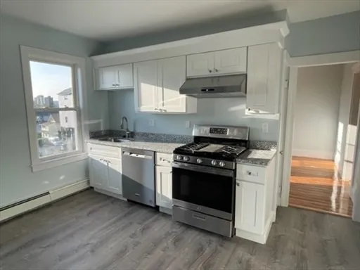 a kitchen with a stove white cabinetry and a sink