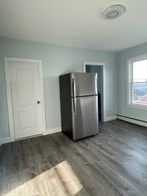 a view of a refrigerator in kitchen and an empty room with wooden floor windows
