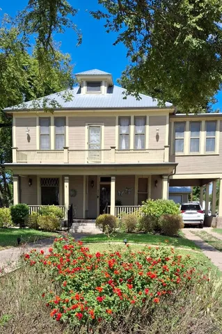 a front view of a house with lots of flowers and trees