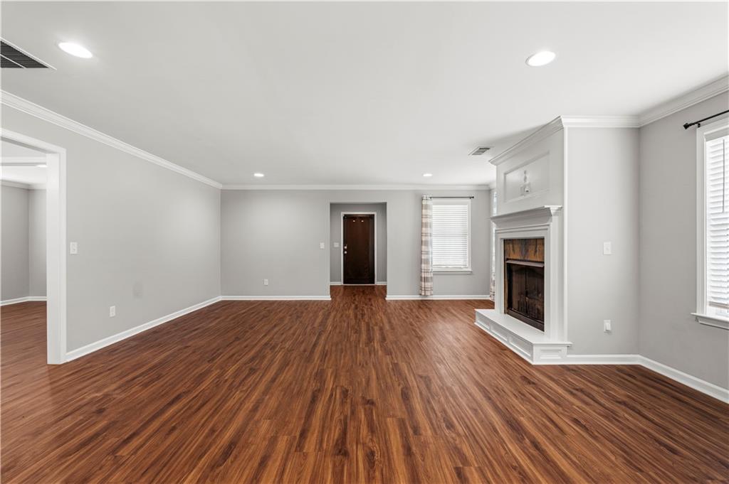 Spacious living area featuring wood-finish flooring, a traditional fireplace with a white mantel, recessed lighting, and ample natural light from multiple windows
