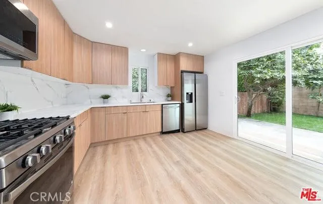 a kitchen with stainless steel appliances granite countertop a stove a sink dishwasher and a refrigerator with wooden floor