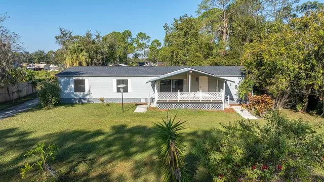 a white house with a large pool plants and large trees