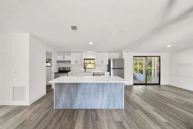 a large kitchen with stainless steel appliances granite countertop a large counter top a stove and a wooden floors