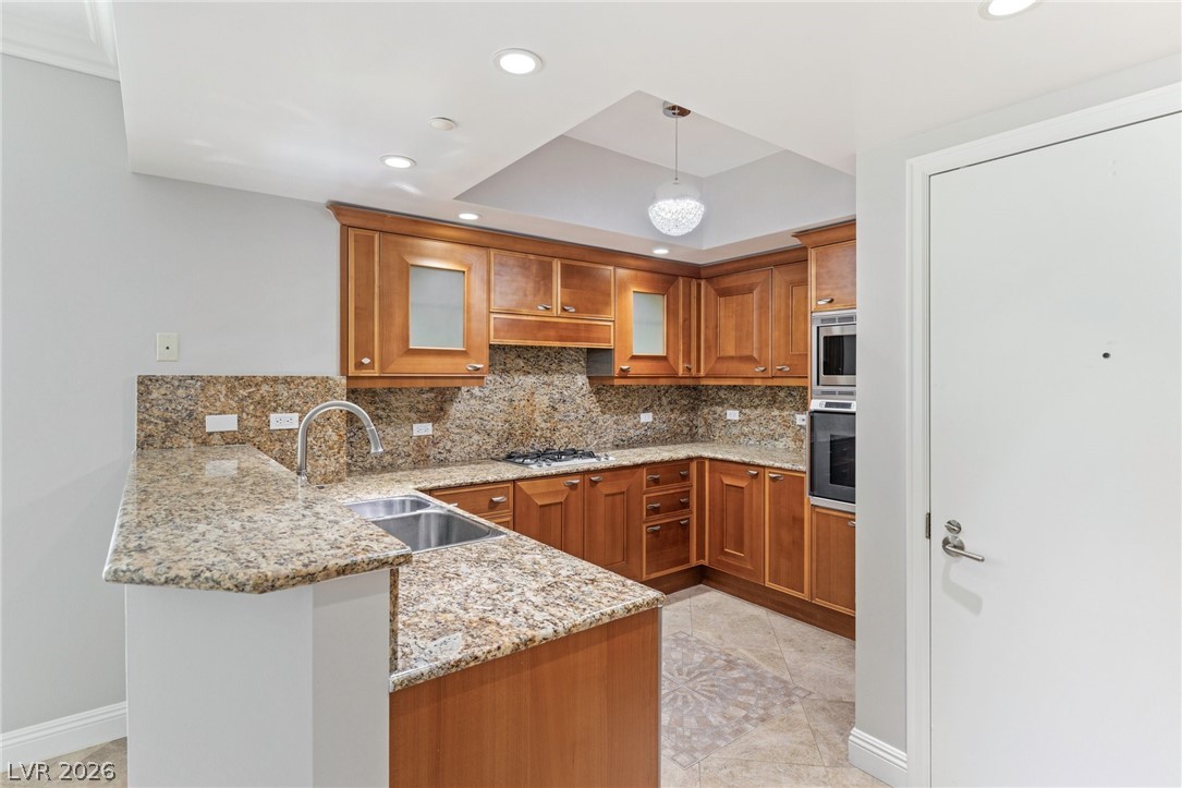 2777 Paradise Road, Unit 901 Las Vegas, NV 89109 - Photo 4 of 27 Kitchen featuring backsplash, a sink, a peninsula, appliances with stainless steel finishes, and brown cabinetry