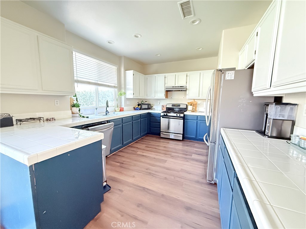 1652 Apollo Way Beaumont, CA 92223 - Photo 3 of 25 a large kitchen with stainless steel appliances kitchen island granite countertop a sink dishwasher a stove a refrigerator a washer and dryer with wooden cabinets