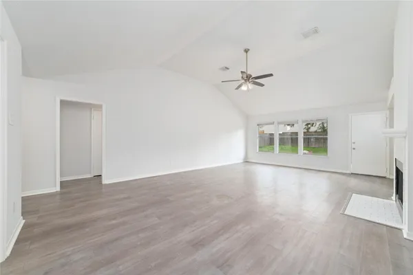 an empty room with wooden floor ceiling fan and windows