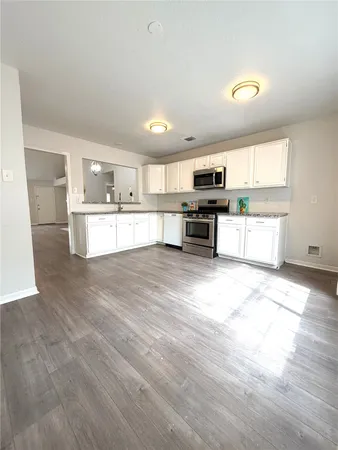 a large kitchen with kitchen island granite countertop a stove a sink a refrigerator and white cabinets with wooden floor