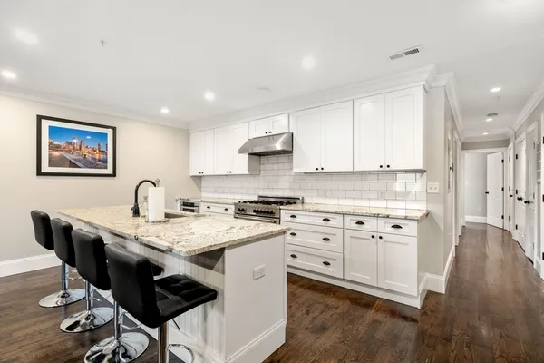 a kitchen with stainless steel appliances granite countertop a stove top oven a sink a dining table and chairs with wooden floor
