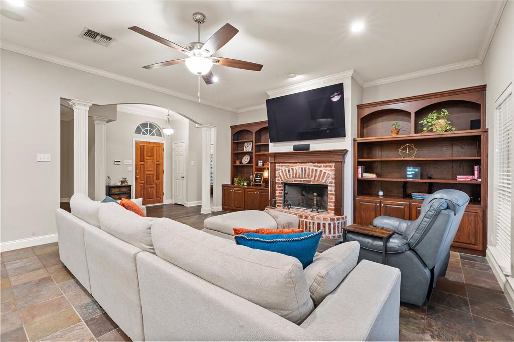 517 Chado Lane Robinson, TX 76706 - Photo 7 of 40 Living area with stone tile flooring, arched walkways, a fireplace, a ceiling fan, and crown molding
