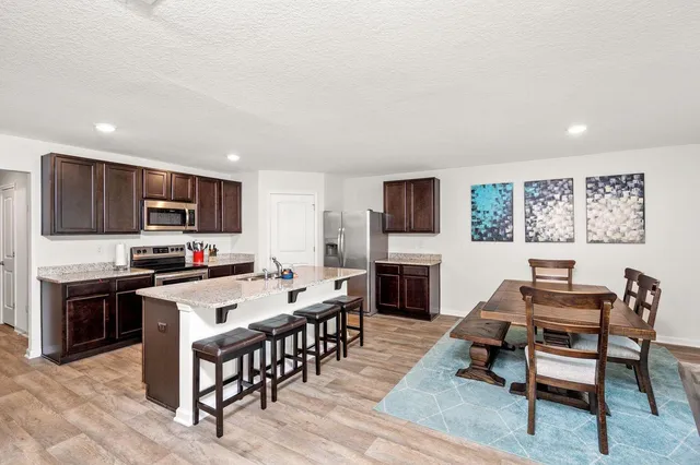 a kitchen with granite countertop a stove top oven a sink dishwasher a dining table and chairs with wooden floor