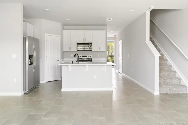 a large kitchen with stainless steel appliances a refrigerator a sink a stove top oven and white cabinets