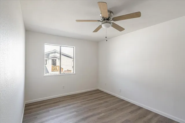 an empty room with wooden floor fan and windows
