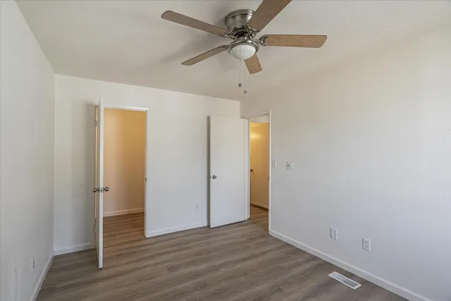 an empty room with wooden floor fan and windows