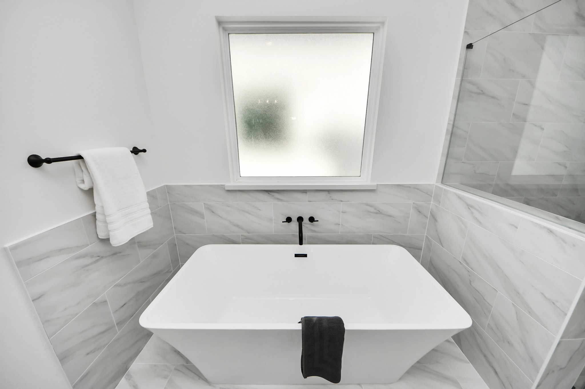 717 Marcella Street, Unit E Houston, TX 77091 - Photo 20 of 25 This bathroom features a modern, freestanding bathtub with sleek black fixtures and elegant gray marble tile. A frosted window provides privacy and natural light, while a towel rack adds convenience.