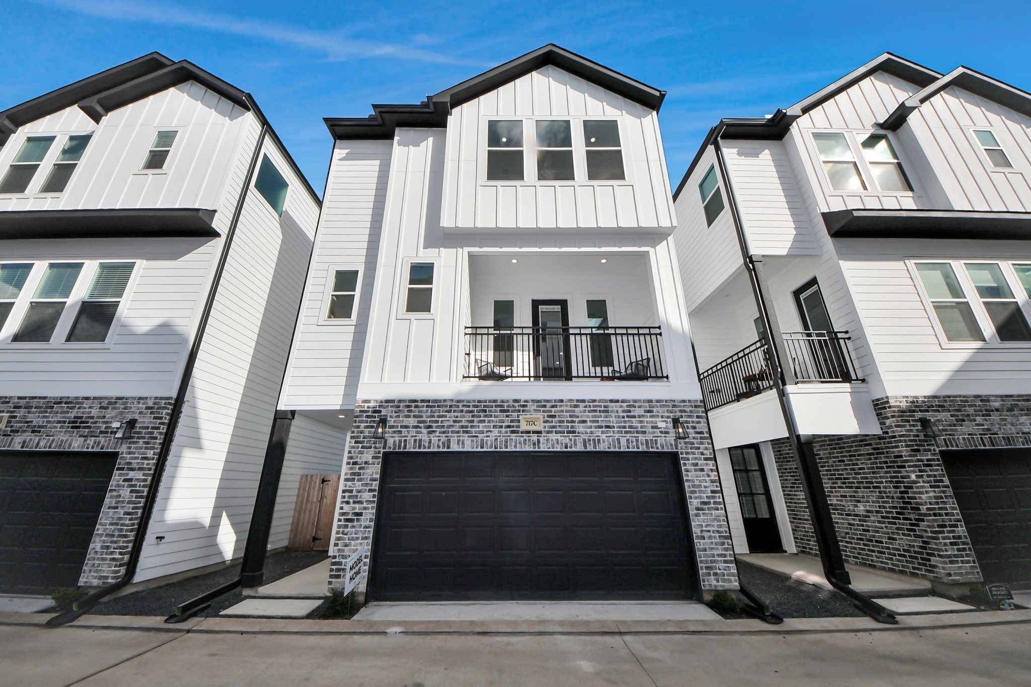 717 Marcella Street, Unit E Houston, TX 77091 - Photo 2 of 25 Modern three-story townhouse with a sleek design, featuring a white exterior accented by brickwork. Includes a two-car garage and a small balcony, offering a stylish urban living option.