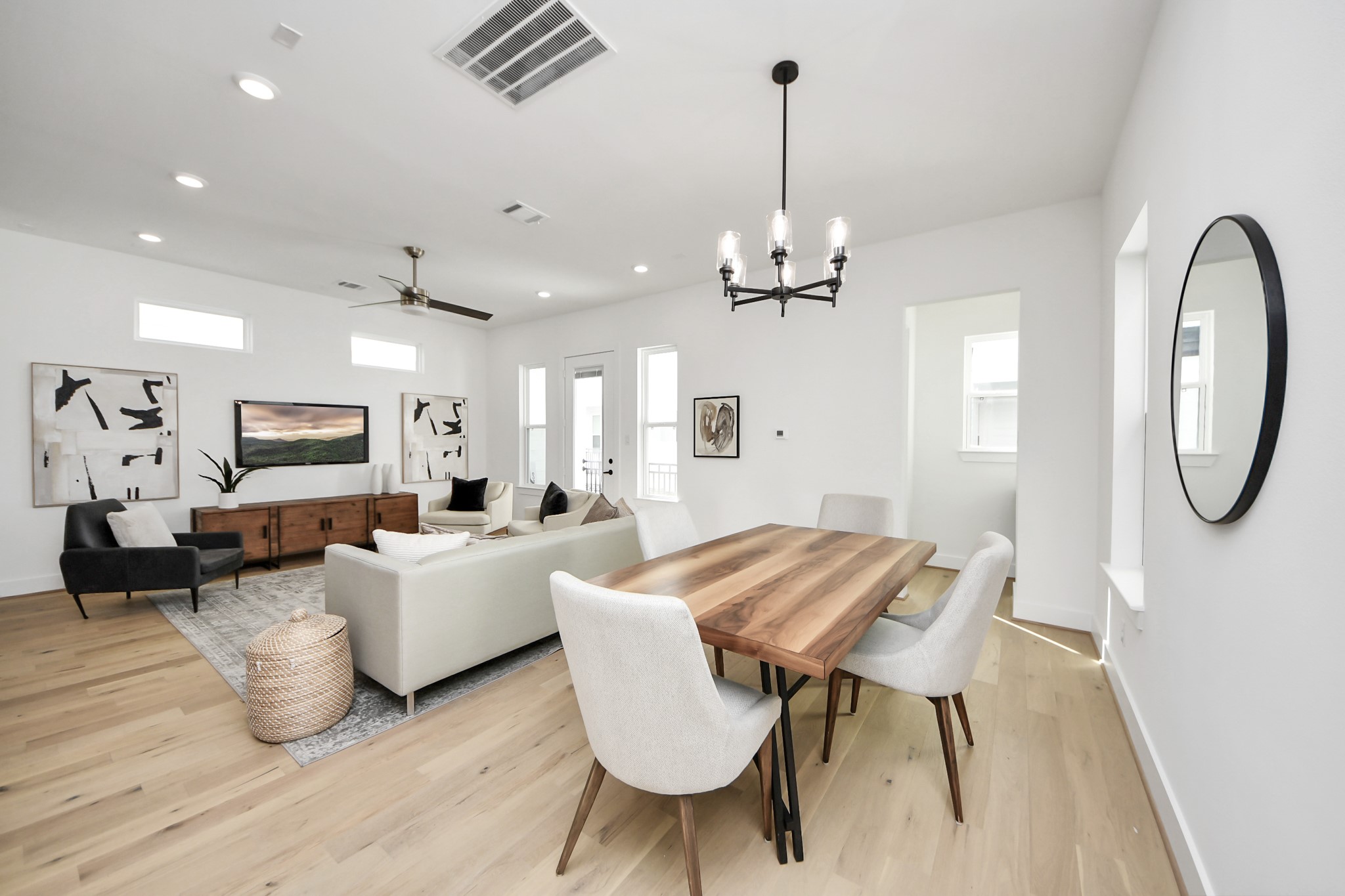 717 Marcella Street, Unit E Houston, TX 77091 - Photo 8 of 25 This photo showcases a modern open-concept living and dining area with light wood flooring and white walls. The space is bright, featuring a dining table with upholstered chairs, a comfortable seating area with a sofa and armchairs, and contemporary decor. Large windows and a glass door allow for ample natural light.