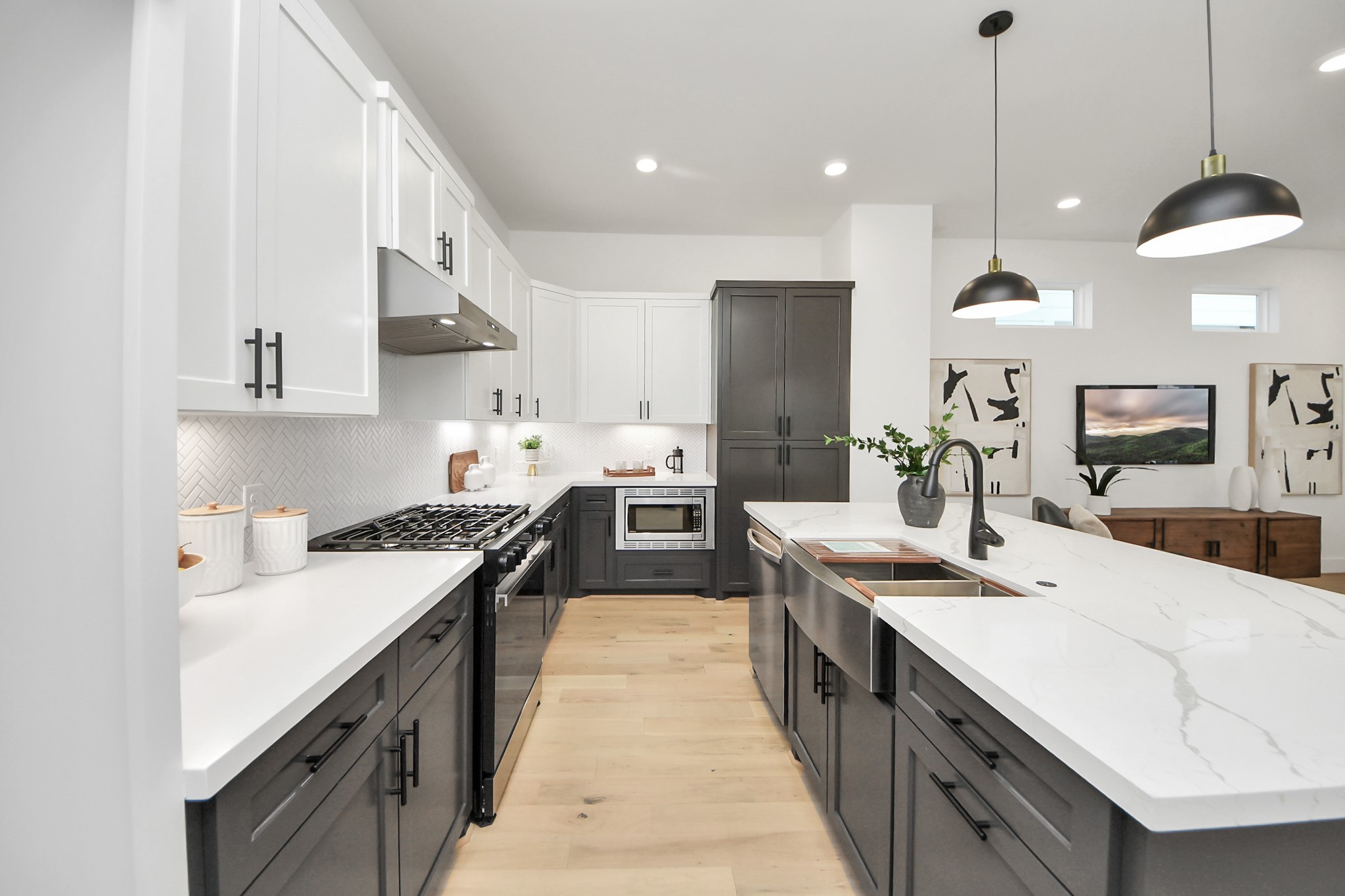 717 Marcella Street, Unit E Houston, TX 77091 - Photo 9 of 25 This modern kitchen features sleek white and dark cabinetry, a large island with a marble countertop, and stainless steel appliances. It has an open layout with stylish pendant lighting, creating a bright and inviting space perfect for cooking and entertaining.