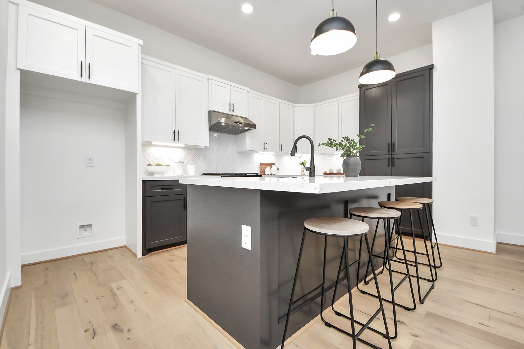 717 Marcella Street, Unit E Houston, TX 77091 - Photo 10 of 25 This modern kitchen features sleek white cabinets, a large black island with a marble countertop, and stylish pendant lighting. The space includes bar seating and has light wood flooring for a bright, contemporary feel.