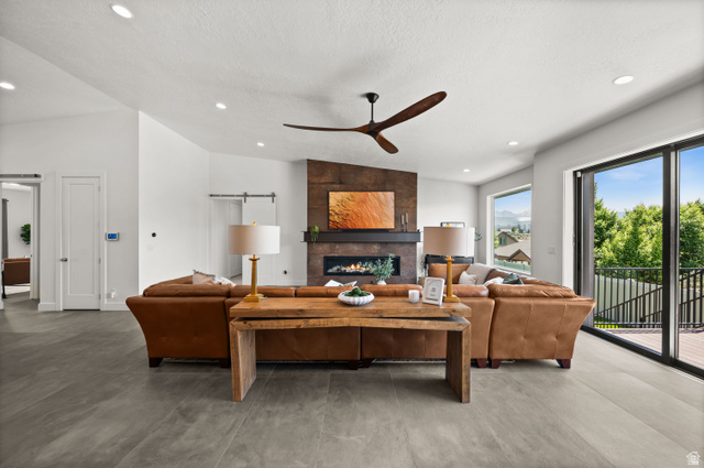 507 West Windmill Gate Cove Draper, UT 84020 - Photo 9 of 46 Living room featuring concrete floors, a ceiling fan, a tiled fireplace, lofted ceiling, and recessed lighting