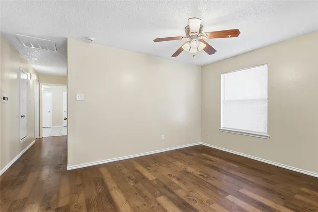 an empty room with wooden floor fan and windows