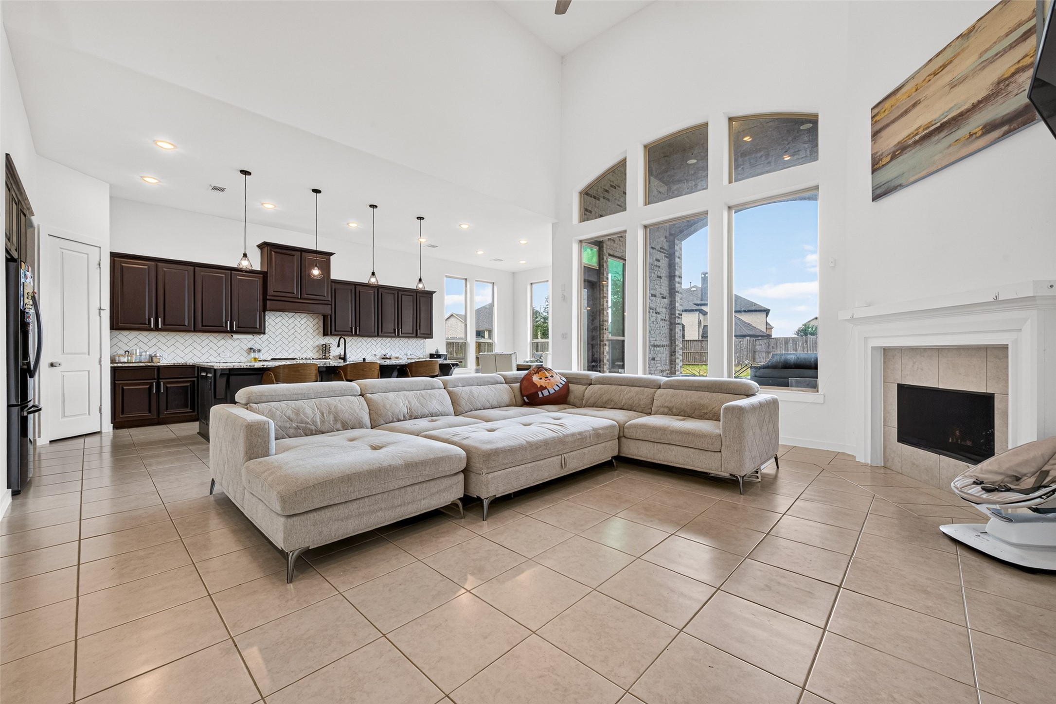 10114 Brush Way Rosharon, TX 77583 - Photo 14 of 50 Spacious living area with high ceilings, abundant natural light from large windows, and an elegant fireplace. The open layout flows seamlessly into a modern kitchen with dark cabinetry and stylish pendant lighting.