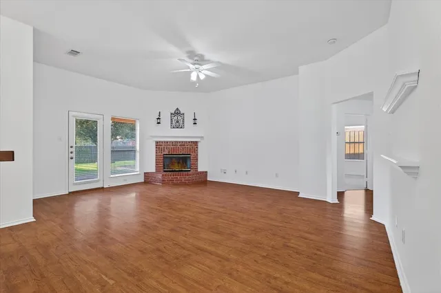 an empty room with wooden floor fireplace and windows