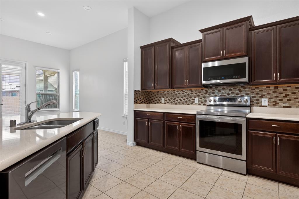 8728 Maple Ridge Trail Fort Worth, TX 76244 - Photo 14 of 40 Kitchen featuring an island with an undermount sink, dark wood-finish cabinetry, stainless steel appliances, a mosaic tile backsplash, and light-toned countertops