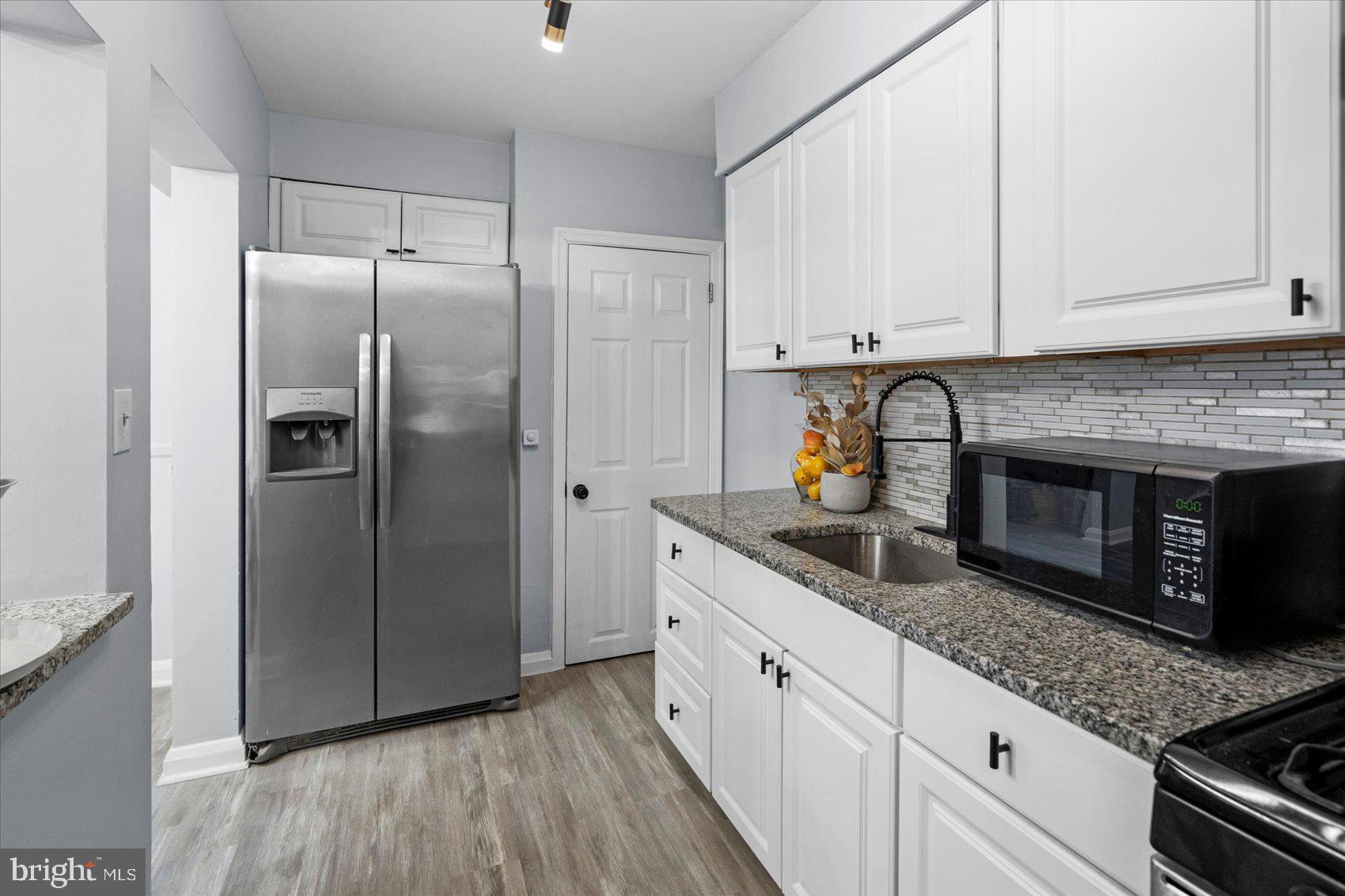 8411 Kavanagh Road Baltimore, MD 21222 - Photo 12 of 48 a kitchen with stainless steel appliances granite countertop a refrigerator a stove and white cabinets with wooden floor