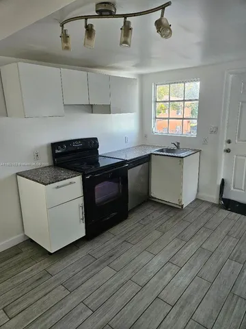 a kitchen with granite countertop a stove a sink and white cabinets with wooden floor