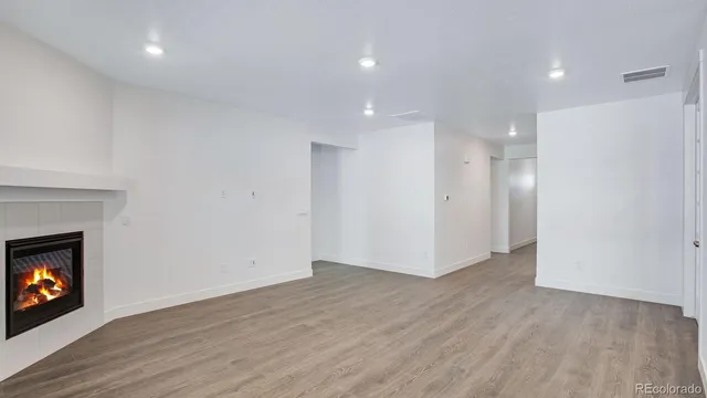 a view of an empty room with wooden floor fireplace and a window