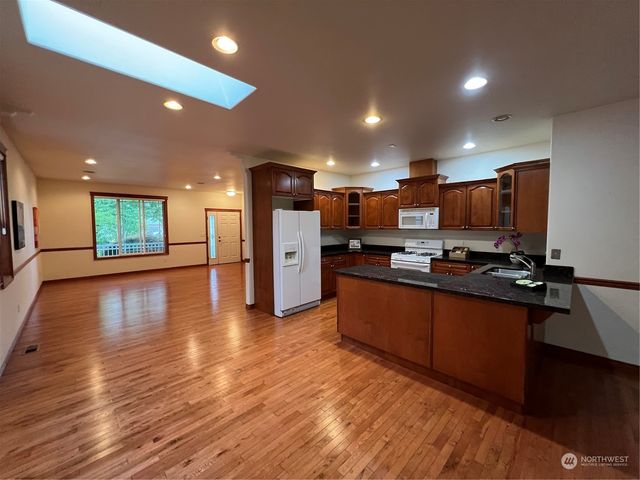a view of kitchen with stainless steel appliances granite countertop a stove top oven a sink dishwasher a refrigerator and a dining table with wooden floor