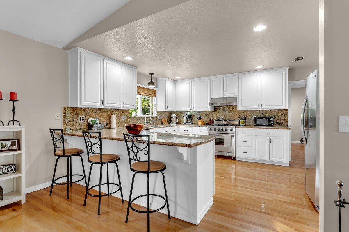 12269 Dry Creek Road Bella Vista, CA 96008 - Photo 13 of 74 a kitchen with white cabinets stove and chair with wooden floor
