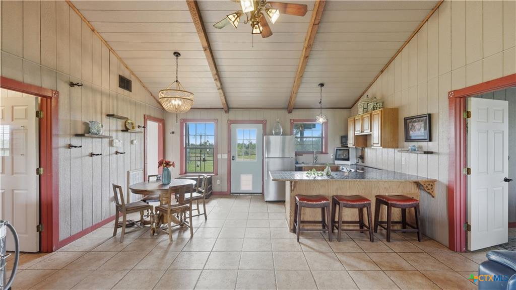 127 Offer Llano, TX 78643 - Photo 8 of 40 Open-concept kitchen and dining area featuring tile flooring, exposed ceiling beams, wood-finish cabinetry, and a peninsula with bar seating