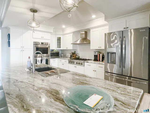 a kitchen with stainless steel appliances granite countertop a refrigerator a stove a sink dishwasher a dining table and chairs with wooden floor