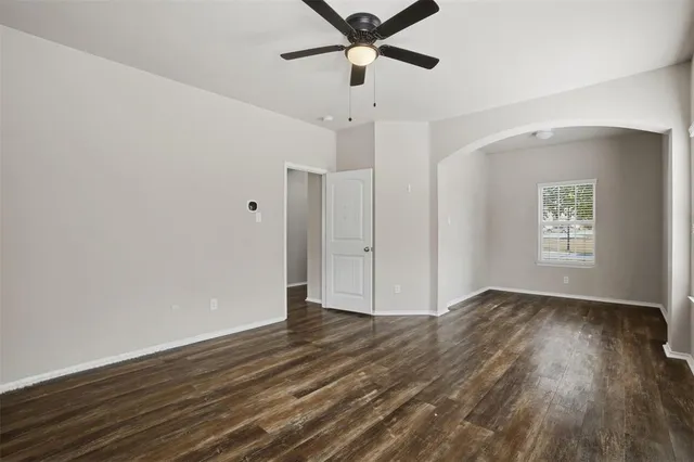 a view of an empty room with wooden floor and a ceiling fan