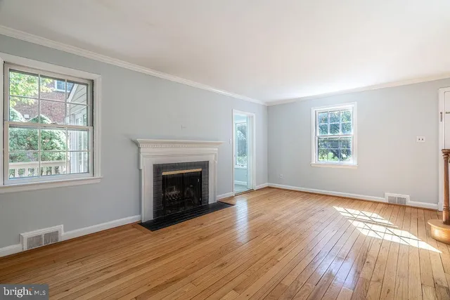 an empty room with wooden floor fireplace and windows