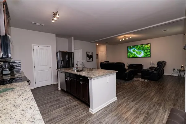 a open kitchen with stainless steel appliances granite countertop a stove top oven a refrigerator a sink dishwasher with a dining table and chairs with wooden floor