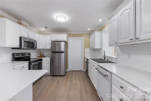 a kitchen with granite countertop wooden floors stainless steel appliances a sink and a counter space