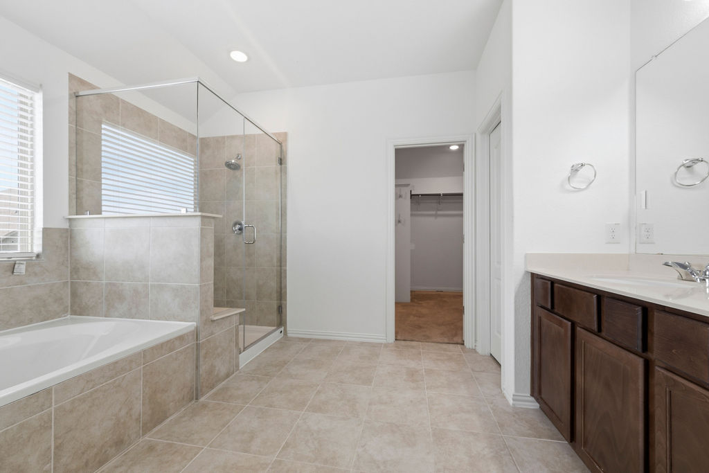 1005 Ridge Runner Drive Georgetown, TX 78628 - Photo 27 of 32 Spacious bathroom featuring a glass-enclosed shower, a separate soaking tub, dual vanities with integrated sinks, wood-finish cabinetry, and neutral tile flooring