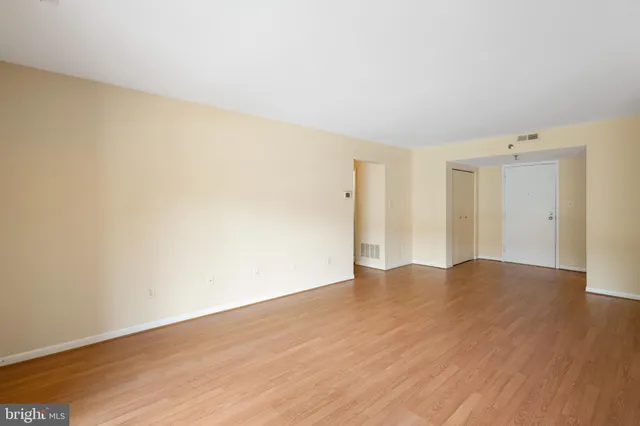 a view of empty room with wooden floor and kitchen