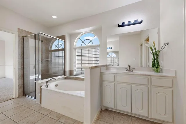 a spacious en suite bathroom with a granite countertop tub a double vanity sink a window and a mirror